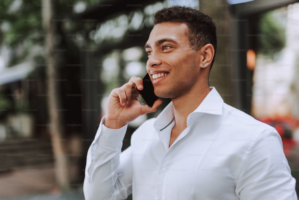 Close up portrait of handsome afro american guy talking on cellphone outdoors. He looking away and smiling