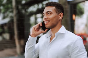 Retrato de primer plano de un chico afroamericano guapo hablando por teléfono celular al aire libre. Apartó la mirada y sonrió