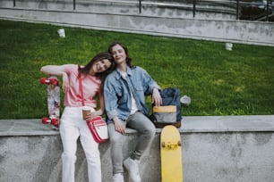 Urban lifestyle and sport activity concept. Portrait of young happy hipster ladies relaxing on parapet after skateboarding. Copy space on right