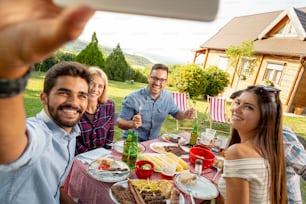 Gruppo di amici che organizzano una festa barbecue in cortile, pranzano all'aperto e si divertono a scattare selfie