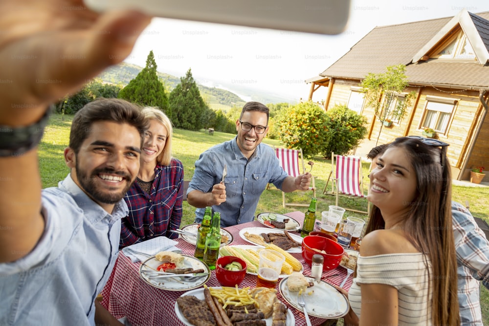 Group of friends having a backyard barbecue party, eating lunch outdoors and having fun taking selfies