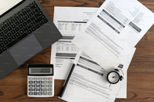 노트북 컴퓨터, 문서, 재정 청구서, 알람 시계, 계산기 및 사무실의 나무 테이블에 있는 문구의 상위 뷰