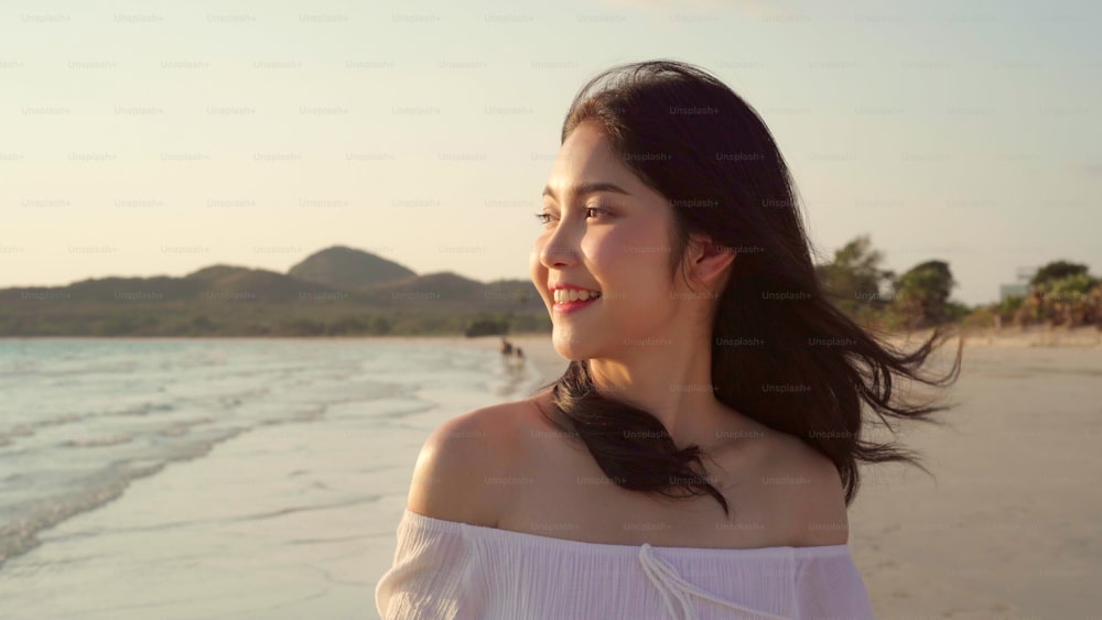 Young Asian woman walking on beach. Beautiful female happy relax walking on beach near sea when sunset in evening. Lifestyle women travel on beach concept.