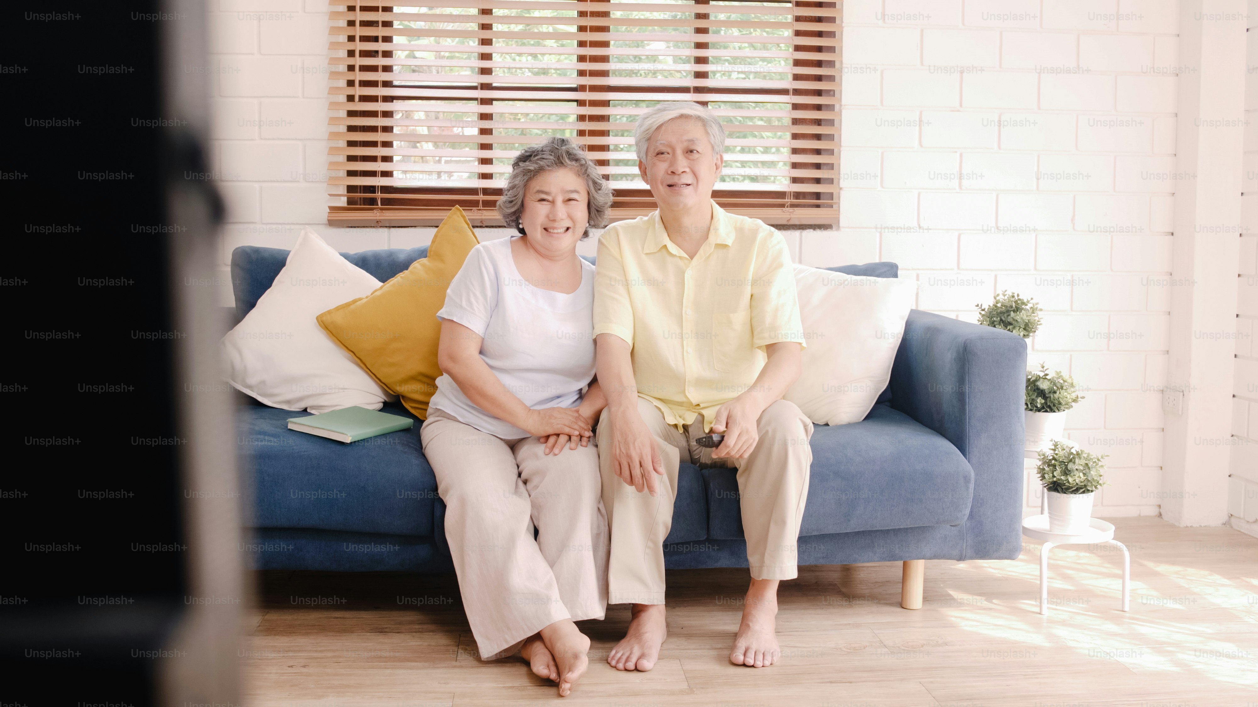 Asian elderly couple watching television in living room at home, sweet couple enjoy love moment while lying on the sofa when relaxed at home. Enjoying time lifestyle senior family at home concept.