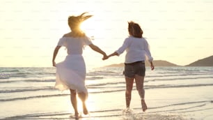 Junges asiatisches lesbisches Paar läuft am Strand. Schöne Frauen Freunde glücklich entspannen sich Spaß am Strand in der Nähe des Meeres, wenn Sonnenuntergang am Abend. Lifestyle lesbisches Paar Reisen am Strand Konzept.