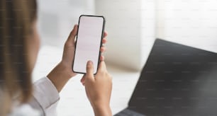 Vista de primer plano de la mano de la startup femenina en busca de nueva información en un teléfono inteligente de pantalla en blanco