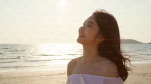 Joven mujer asiática caminando en la playa. Hermosa mujer feliz se relaja caminando en la playa cerca del mar cuando la puesta del sol en la noche. Las mujeres de estilo de vida viajan en el concepto de playa.