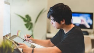 Joven fotógrafo profesional masculino retocando sus fotos con una tableta digital en un lugar de trabajo cómodo