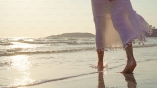 Joven mujer asiática caminando en la playa. Hermosa mujer feliz se relaja caminando en la playa cerca del mar cuando la puesta del sol en la noche. Las mujeres de estilo de vida viajan en el concepto de playa.