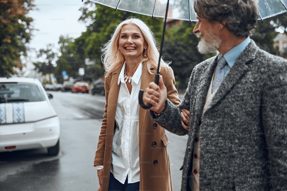 Positive woman laughing and man holding umbrella above them