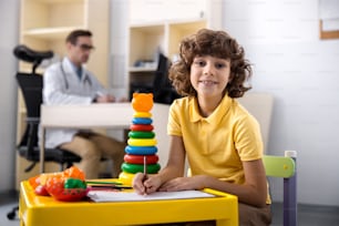 Happy curly child is sitting and drawing in playroom of hospital. Website banner