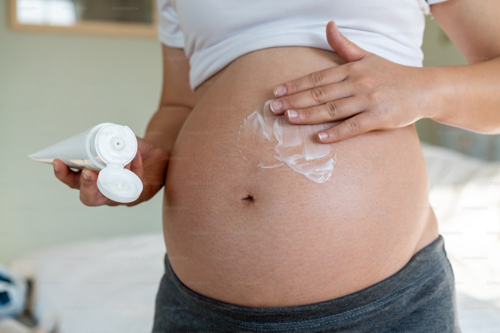 Happy pregnant woman apply skincare cream lotion on pregnant belly to prevent stretch mark. Healthy skin massage treatment and moisture care concept.