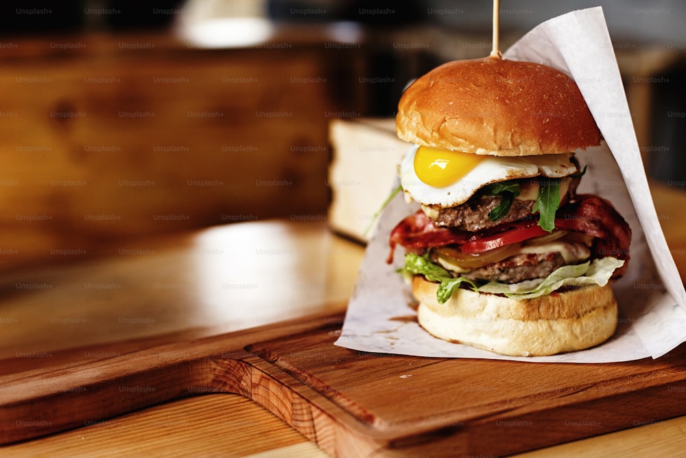 very big juicy burger with vegetables meat cutlet and egg on wooden background, space for text