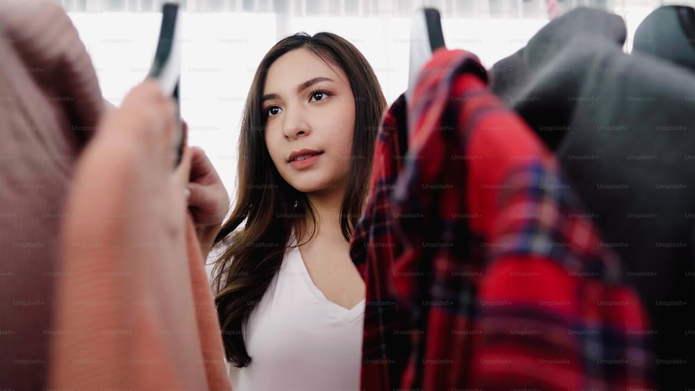 Home wardrobe or clothing shop changing room. Asian young woman choosing her fashion outfit clothes in closet at home or store. Girl think what to wear sweater.