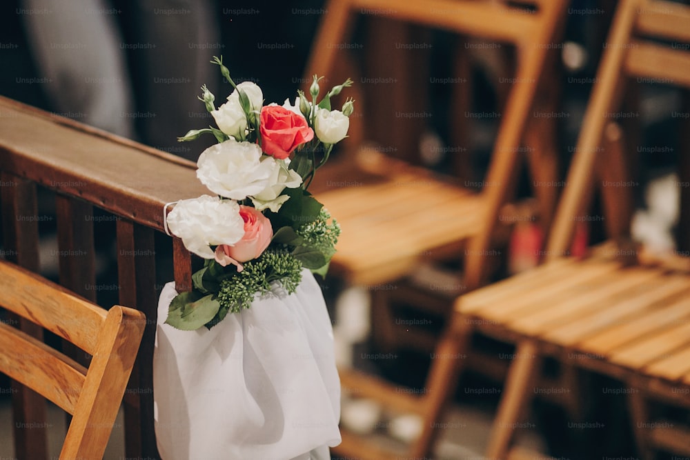 Decoração de casamento elegante de bancos de madeira na igreja para o santo matrimônio. Rosas bonitas e buquês de tule em cadeiras de madeira, arranjo do corredor na igreja