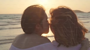 Young Asian lesbian couple kissing near beach. Beautiful women lgbt couple happy relax enjoy love and romantic moment when sunset in evening. Lifestyle lesbian couple travel on beach concept.