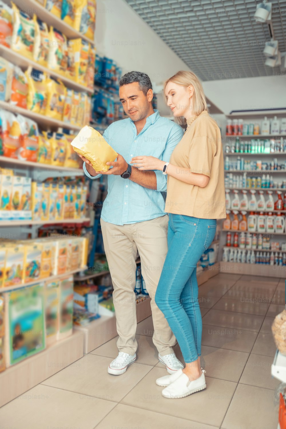 Esposa con jeans. Hermosa esposa rubia con jeans de pie cerca del esposo que toma comida para el perro