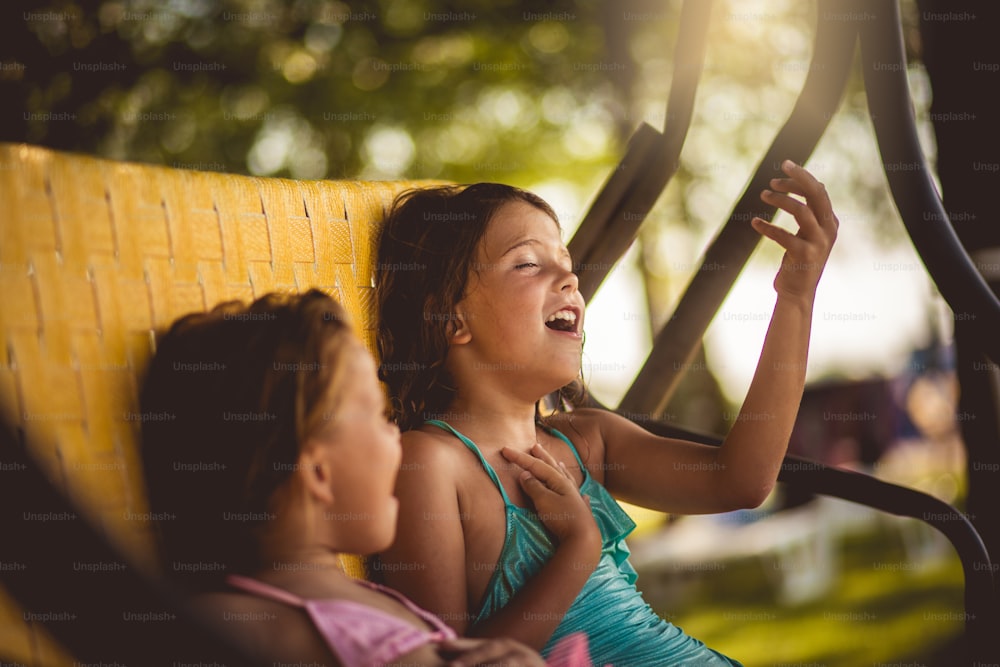 They enjoying together. Two little girl sitting on the bench