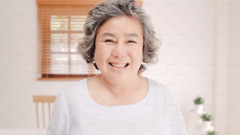 Asian elderly woman feeling happy smiling and looking to camera while relax on the sofa in living room at home. Lifestyle senior women at home concept.