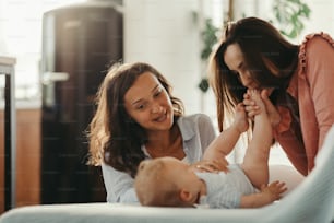 Dos mujeres jóvenes disfrutando con un bebé mientras una de ellas le besa el piecito.