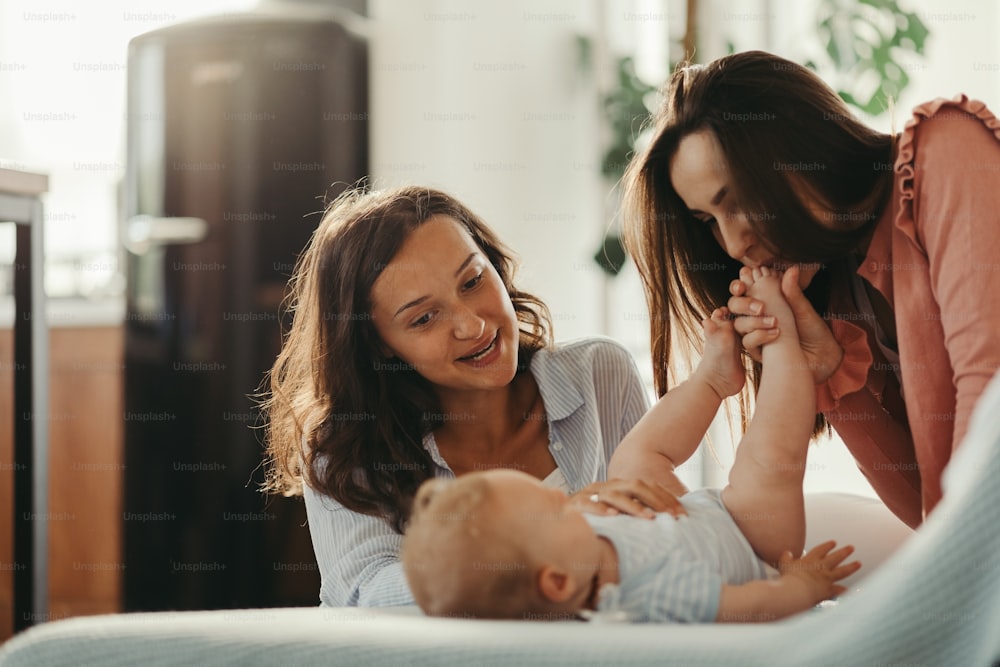 Two young women enjoying with a baby son while one of them is kissing his little foot.