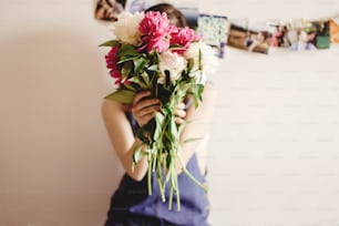 happy woman hipster  holding peony bouquet in front of face sitting on bed in the morning, sweet romantic moment , space for text