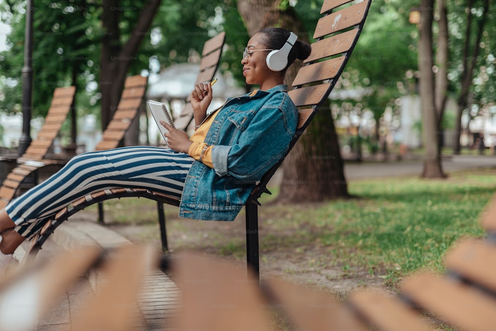 Fröhliche und junge afroamerikanische Frau im Headset verbringt den Sommertag im Stadtpark