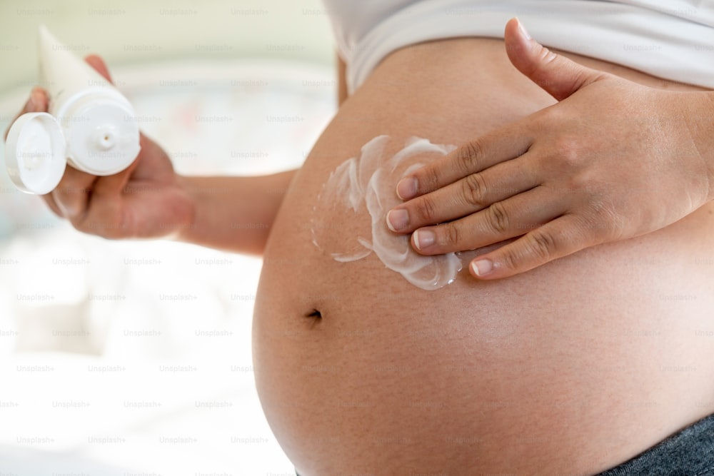 Happy pregnant woman apply skincare cream lotion on pregnant belly to prevent stretch mark. Healthy skin massage treatment and moisture care concept.