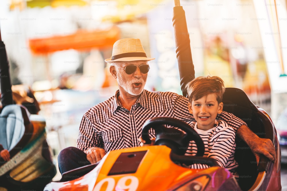 Grandfather and grandson having fun and spending good quality time together in amusement park. They enjoying and smiling while driving bumper car together.