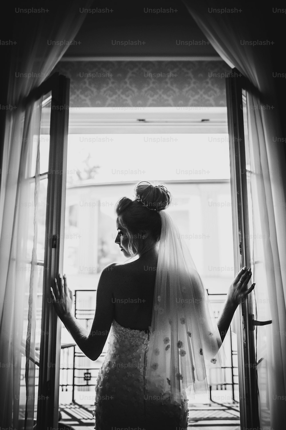 호텔 방의 부드러운 빛에 창문 발코니를 여는 세련된 신부의 실루엣. 흰 가운을 입은 화려한 관능적 인 신부의 뒤. 결혼식 전 아침 준비