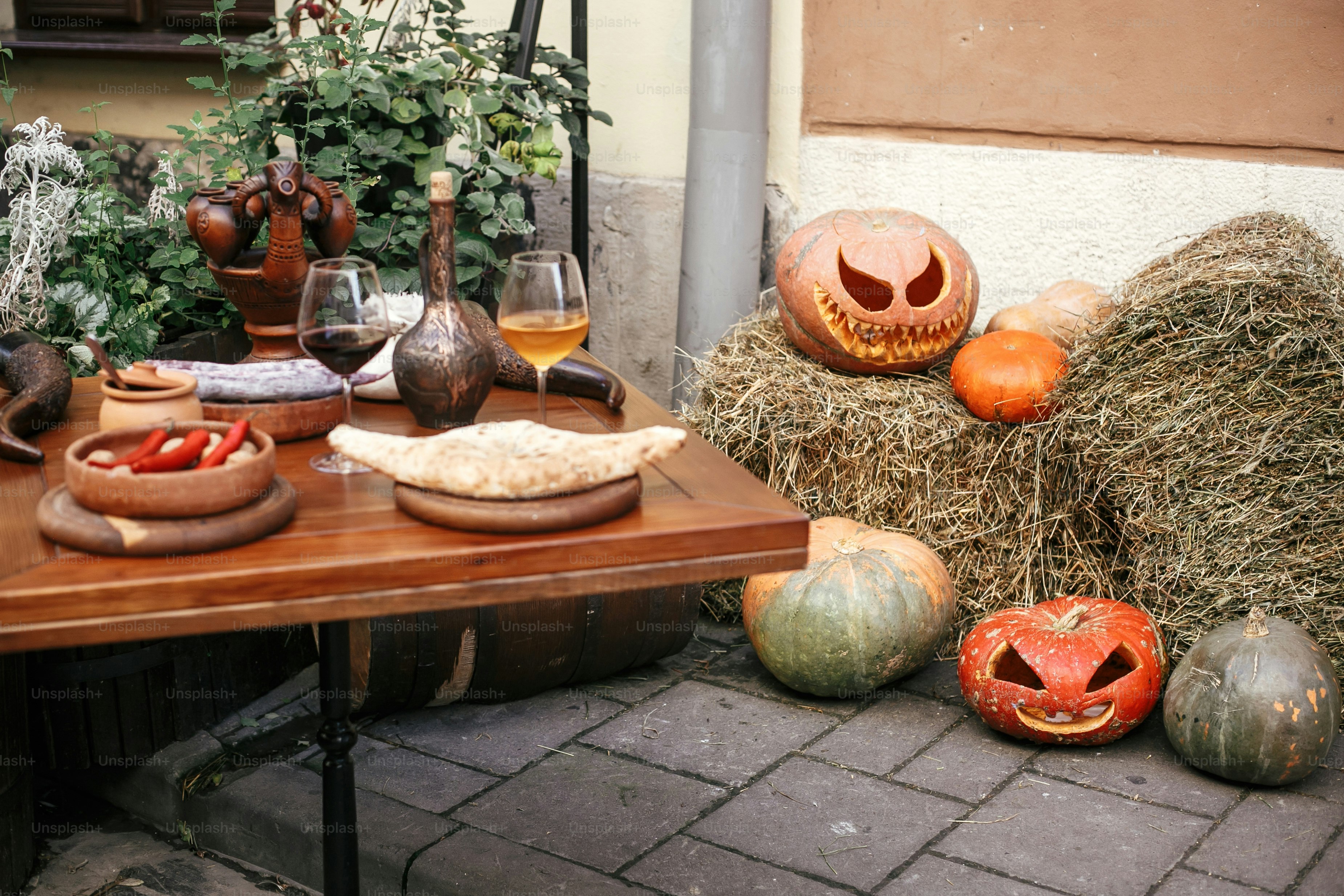 Halloween street decor. Jack o lantern pumpkins on hay in city street, holiday decor of cafe and tables. Autumn market in town. Space for text. Trick or treat. Happy halloween