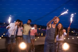 Group of friends enjoying a rooftop party and dancing with sparklers