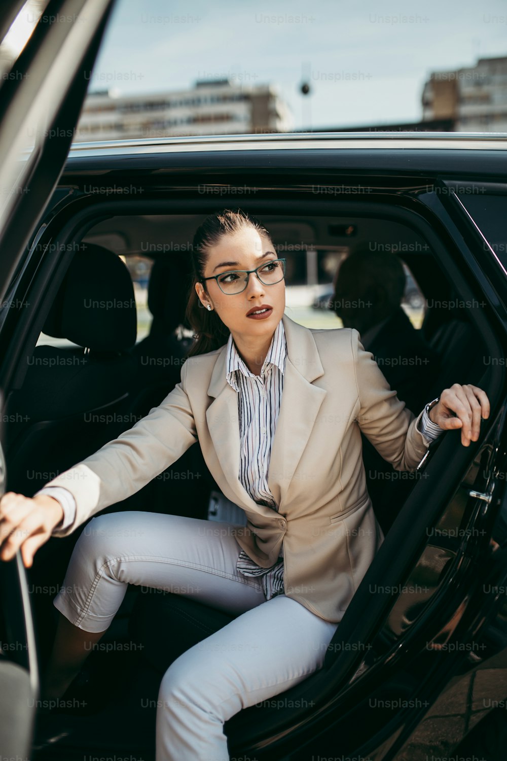 Good looking young business woman sitting on backseat in luxury car. She using her smart phone, smiling and looking outside. Transportation in corporate business concept.