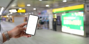 Close-up view of young man holding blank screen smartphone at railway station, blurred background