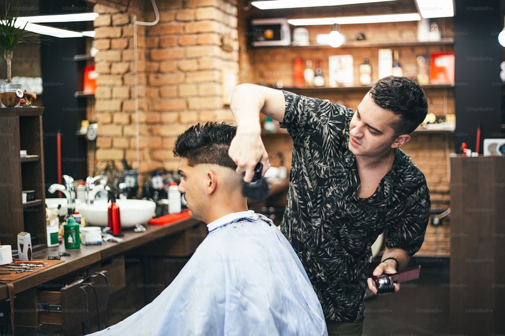 Bearded man with long beard, brutal, caucasian hipster with moustache, with stylish hair, haircut, getting powder on skin with makeup brush by barber or hairdresser hands at barbershop