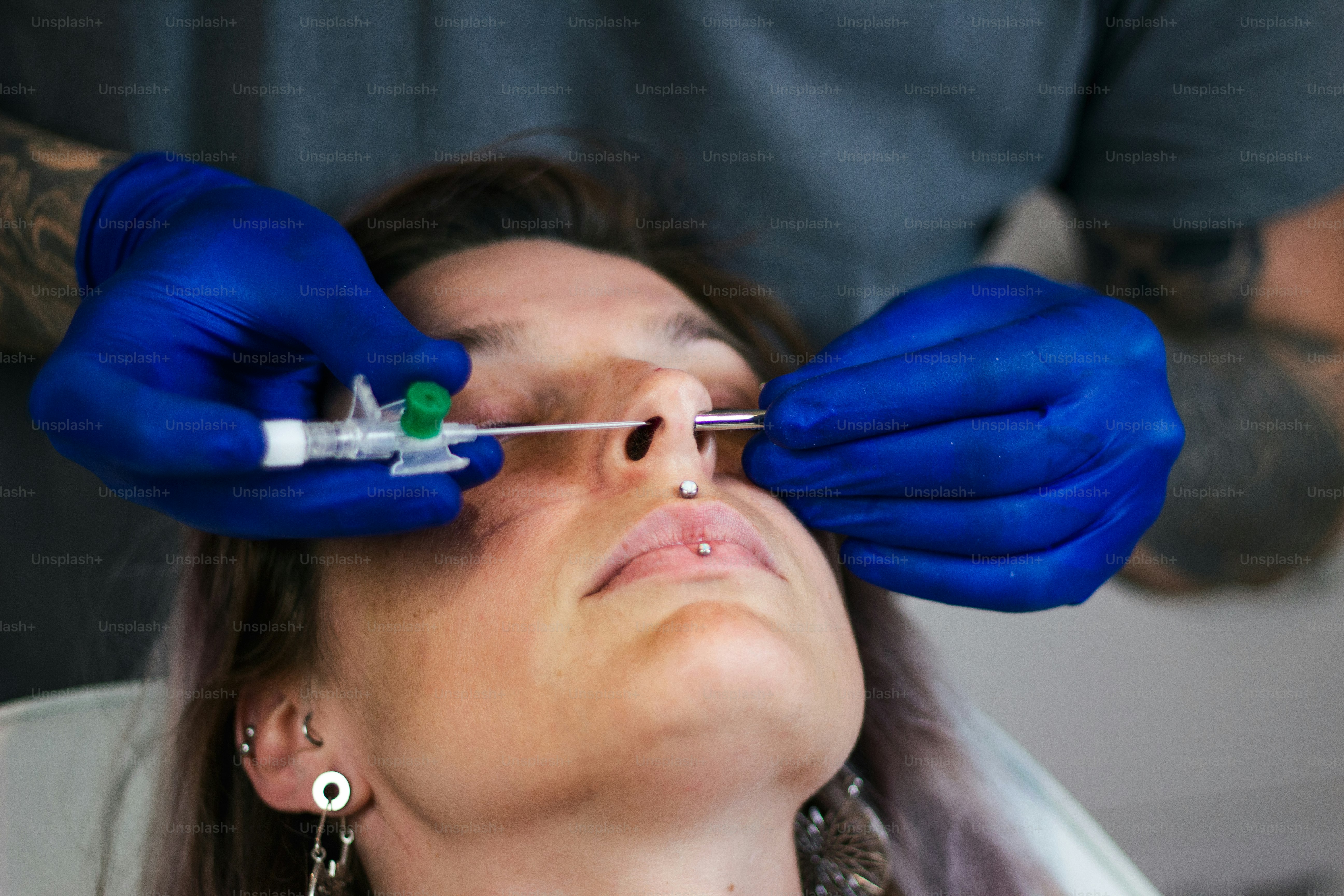 Porträt einer Frau, die sich die Nase stechen lässt. Mann zeigt einen Prozess des Piercings der Nase mit sterilen Neadle und Latexhandschuhen. Nostril Piercing Verfahren