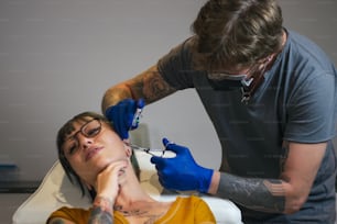 Jovem mulher tendo sua orelha perfurada. Homem mostrando um processo de piercing com equipamentos médicos estéreis e luvas de látex. Procedimento de piercing corporal