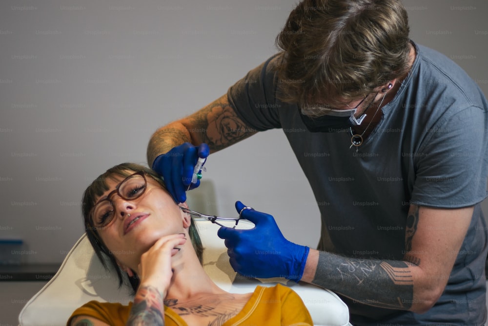 Jeune femme se faisant percer l’oreille. Homme montrant un processus de perçage avec du matériel médical stérile et des gants en latex. Procédure de perçage corporel