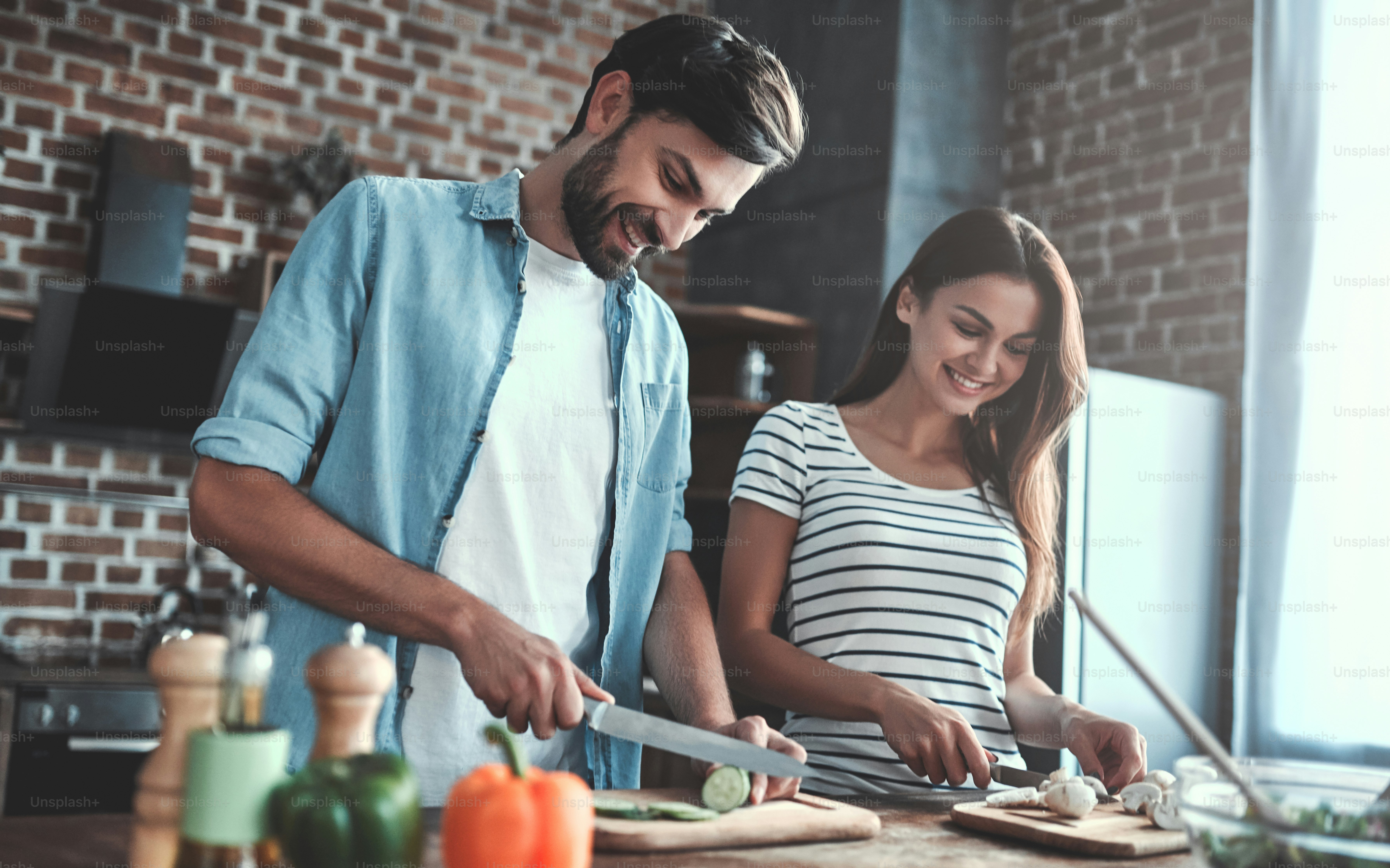 Romantic couple is cooking on kitchen. Handsome man and attractive young woman are having fun together while making salad. Healthy lifestyle concept.