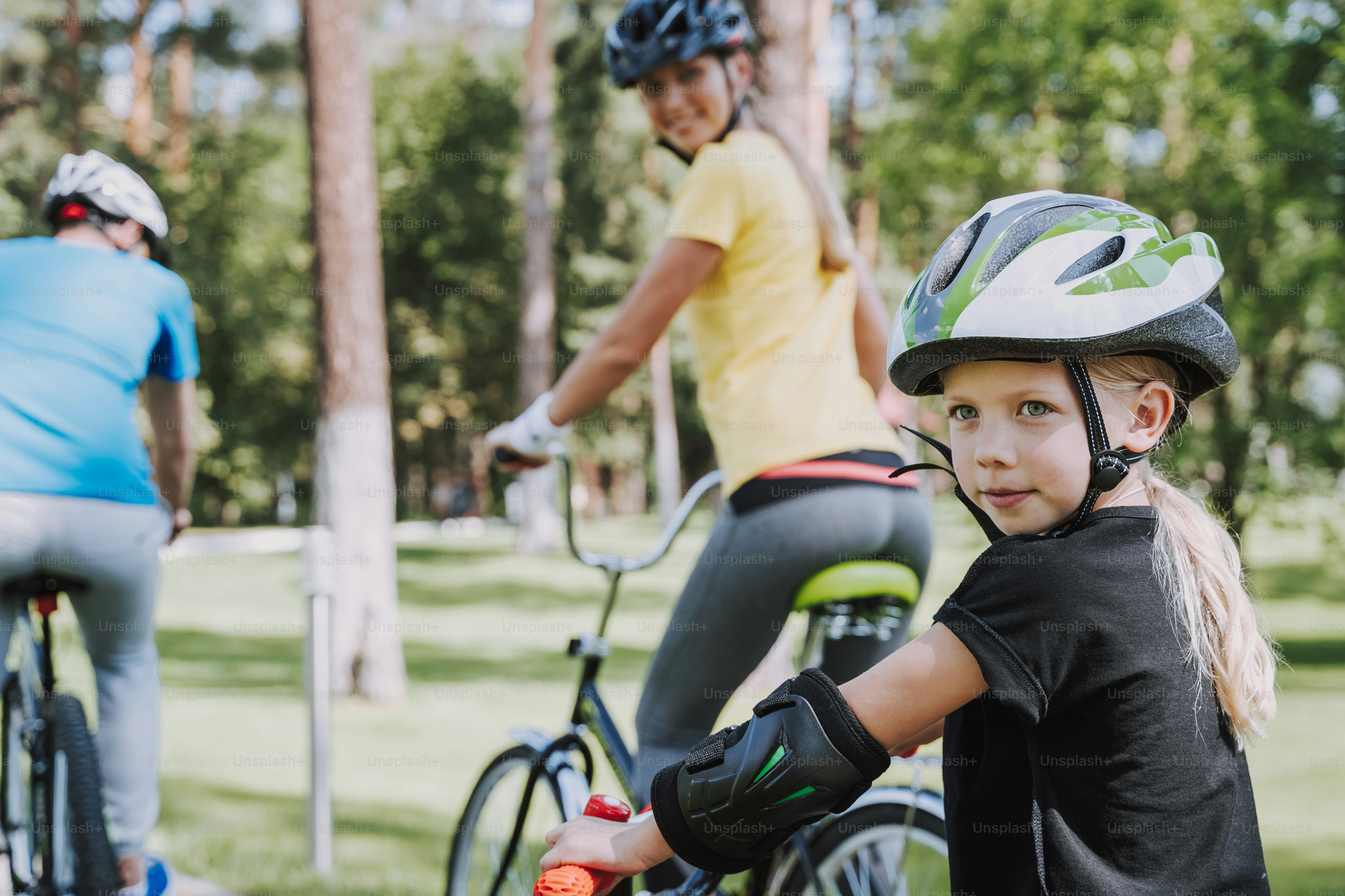 Adorable kid taking a ride on bike with her mother and father. Family and sport activity concept