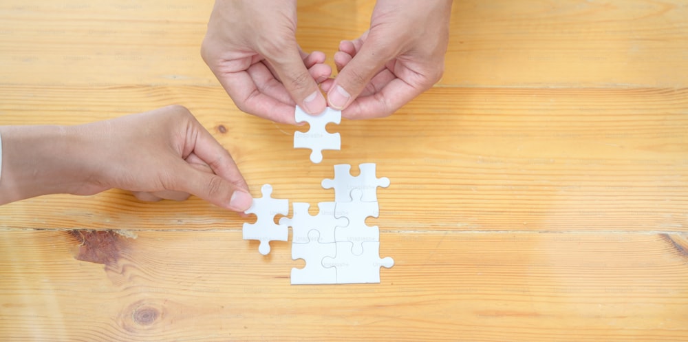 Top view of hands of diverse people assembling jigsaw puzzle together represents teamwork of the group