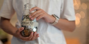 Vista recortada de una joven que sostiene un frasco lleno de monedas para la donación con fondo borroso