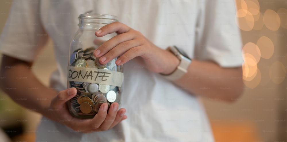 Cropped view of young girl holding a jar full of coins for donation with blurred background