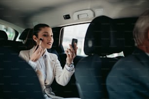 Good looking young business woman sitting on backseat in luxury car and fixing her makeup. Transportation in corporate business concept.