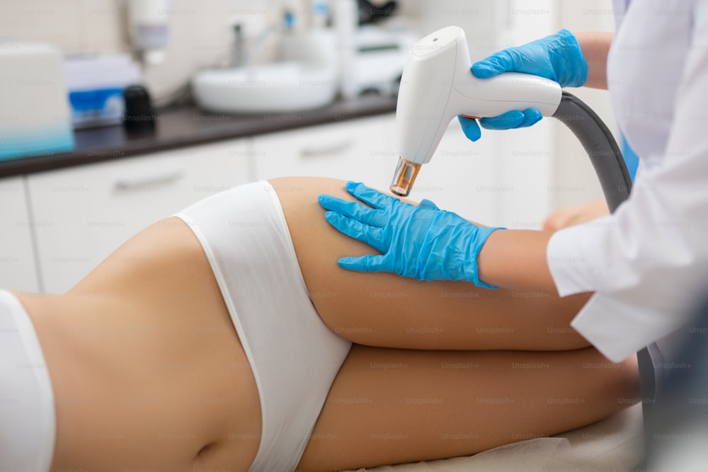 Having all needed procedures. Young woman with slim body lying on a couch in a beauty salon getting laser procedures.