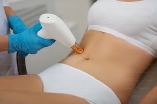 Beautiful body. Belly of a young woman getting laser skin treatment by a cosmetologist wearing rubber gloves.