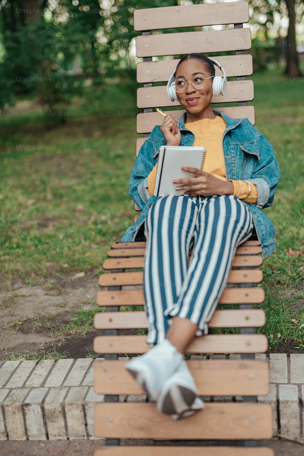 Smiling young african american woman in headset resting at wooden bench in city