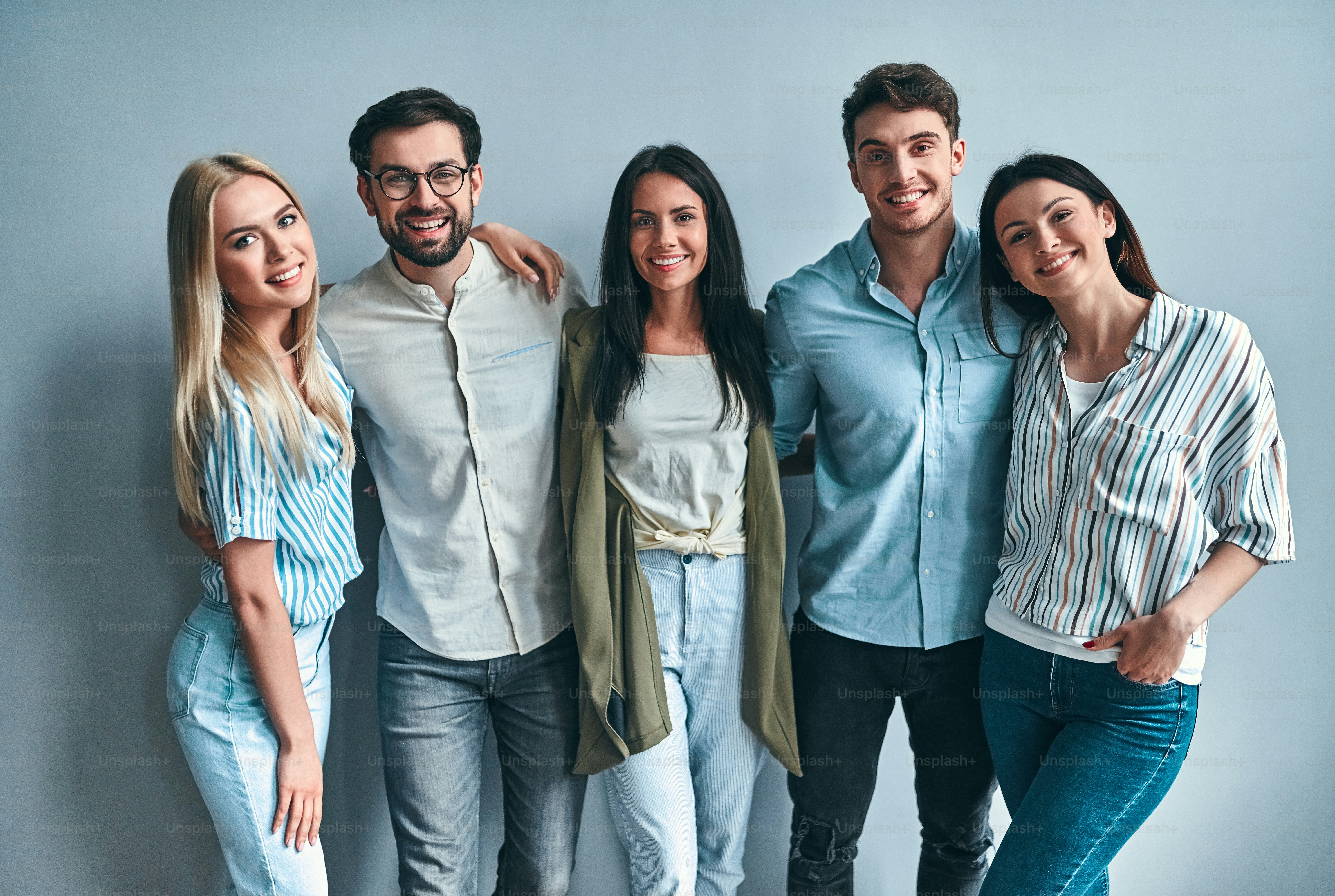 Grupo de jóvenes aislados sobre fondo gris. Jóvenes atractivos que se unen