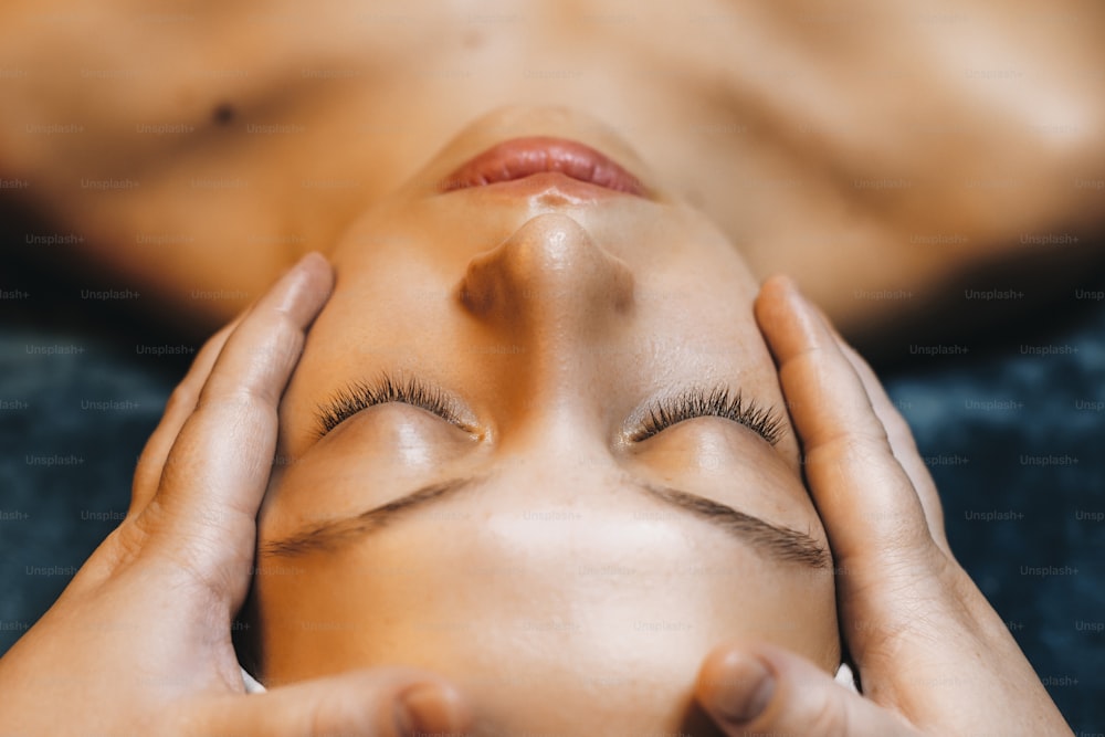 Upper view of a beautiful caucasian woman leaning on a spa bed with closed eyes while having wellness face procedure after alginate mask ina wellness spa center