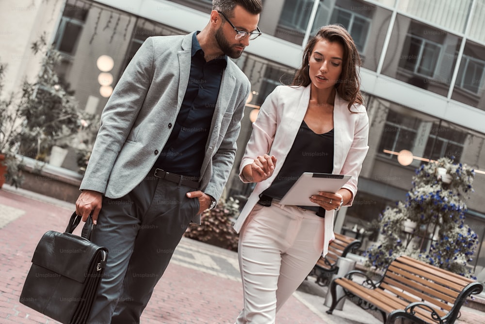 Cropped portrait of man and woman talking to each other while walking to the business center where they work. Woman shows her ideas about new project. Horizontal shot. Dutch angle